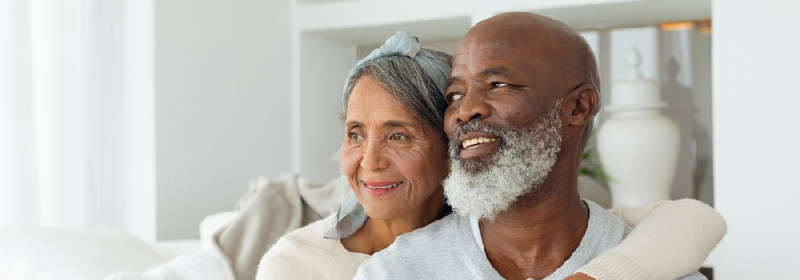 Front view of diverse senior couple sitting on a white couch in beach house